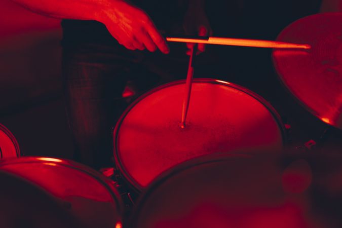 Anonymous man with drumsticks playing on drums in redness