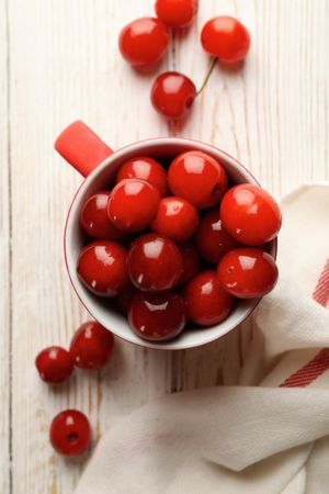 Cup with cherry and towel on wooden background, top view