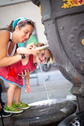 Woman pouring water from fountain for child on street