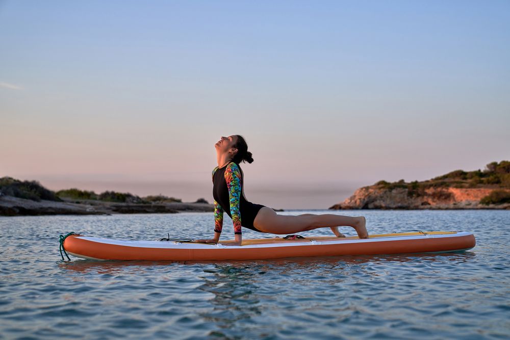 Slim female athlete taking Upward Facing Dog pose on SUP board