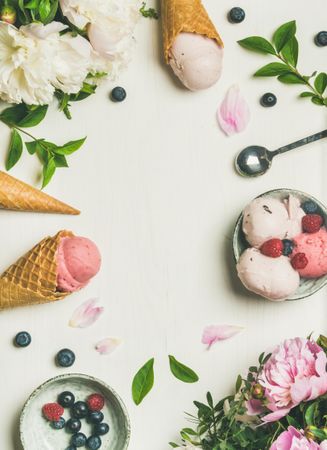 Top view of ice cream scoops, berries and peony flowers on light background