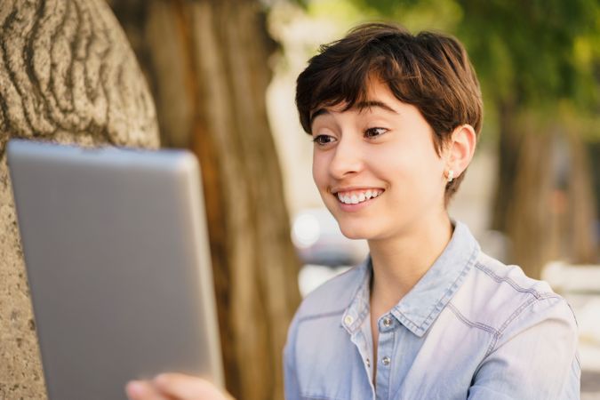 A young person is engaged in a video call while sitting outdoors, enjoying the sunshine