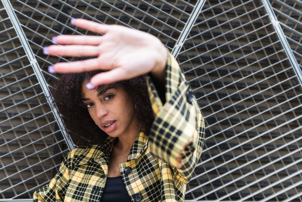 Stylish woman showing stop gesture against grid fence