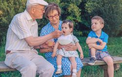 Grandfather feeding baby girl sitting in a bench