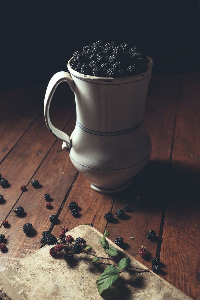 Vintage jag with ripe blackberries on wood and leaves on a old book
