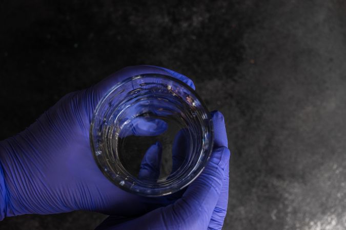 Top view of two hands wearing purple latex gloves holding glass of water