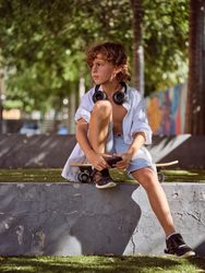Child sitting on skateboard in park and looking away