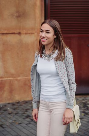 Smiling woman wearing cardigan, pink jeans and satchel bag walking outside