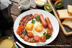 Wooden table with breakfast plate of eggs, tomatoes, sausage and bacon, top view 5wBYW0