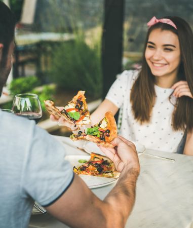Young couple eating pizza al fresco with wine with woman smiling