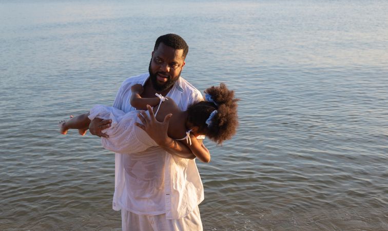 Father holding daughter above the ocean water
