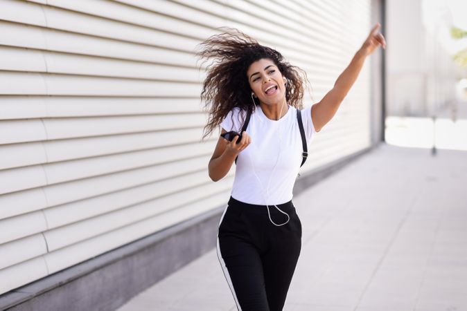 Excited Arab woman in sport clothes with curly hair walking outside while dancing and pointing up