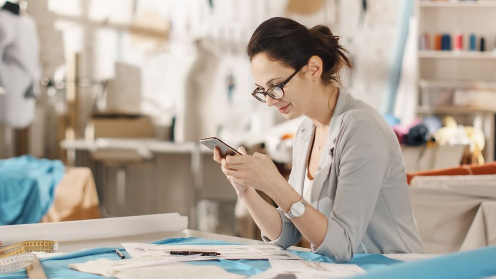 Woman fashion, designer,  Working with Tailoring Mannequin, Adjusting Blouse, Using Smartphone.