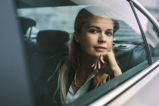Confident young businesswoman sitting on back seat of a taxi and looking outside the window
