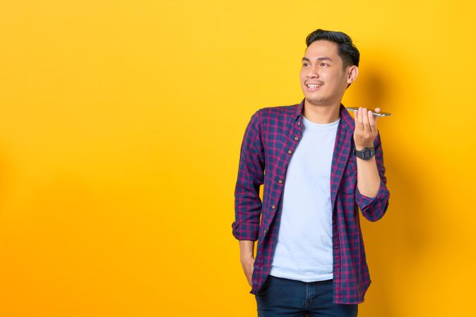 Smiling Asian male listening on cell phone in yellow studio shoot