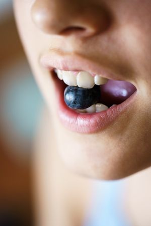 Unrecognizable crop girl holding fresh blueberry between teeth