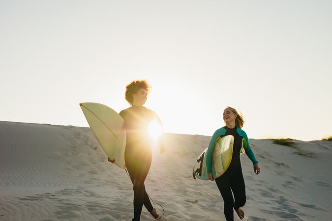 Two female surfers running towards the ocean with long surfboards during sunset