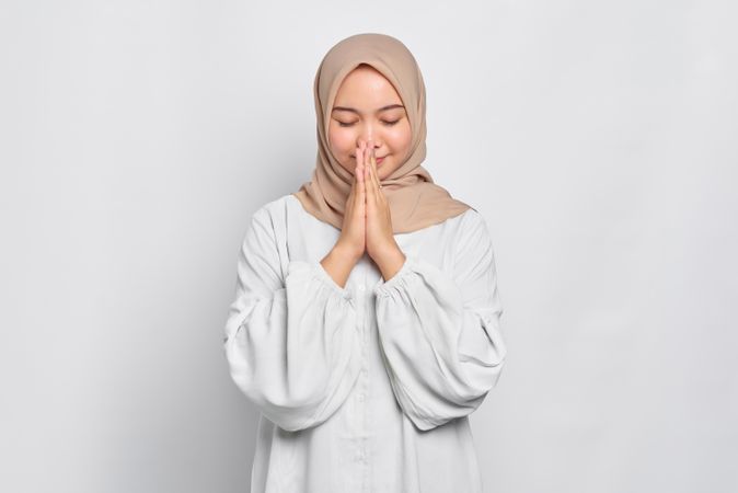 Peaceful Asian female in headscarf with hands together in prayer
