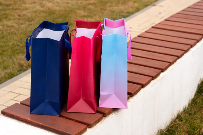 Three empty colorful shopping bags standing on wooden bench.