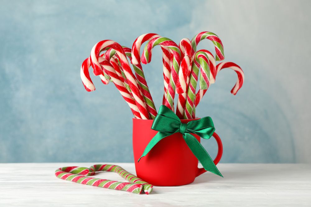 Candy canes in red cup on wooden background, space for text