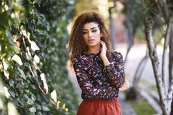 Arab woman wearing casual clothes in the street lined with greenery, copy space