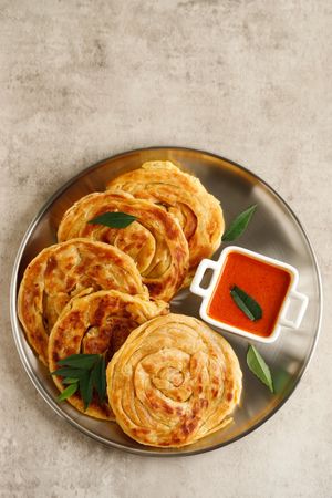 Round plate of roti parata or roti canai with dipping sauce