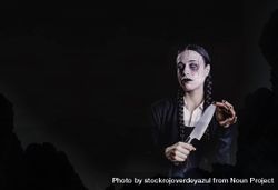 A woman with long braids, with gothic and dark look, plays with a butcher knife 5aXXpK