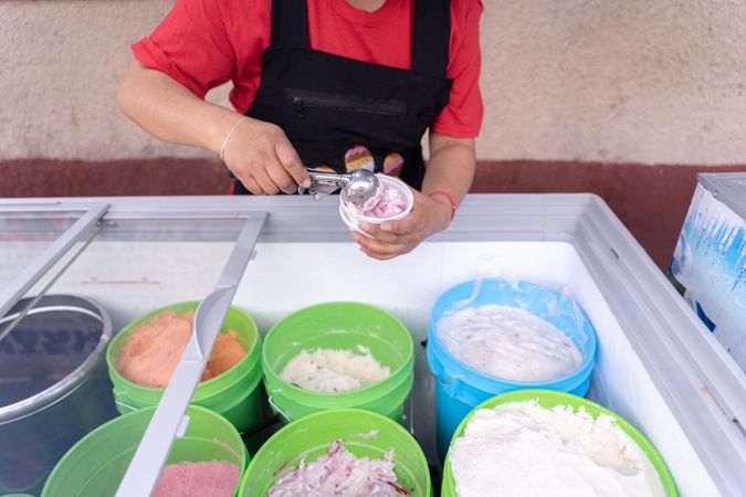 An Hispanic adult woman is serving blackberry and cheese ice cream on a cup in the street