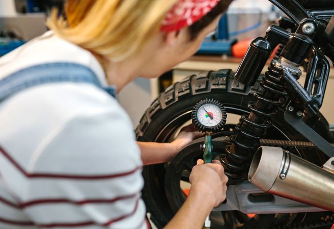 Mechanic woman checking tire air pressure of motorcycle