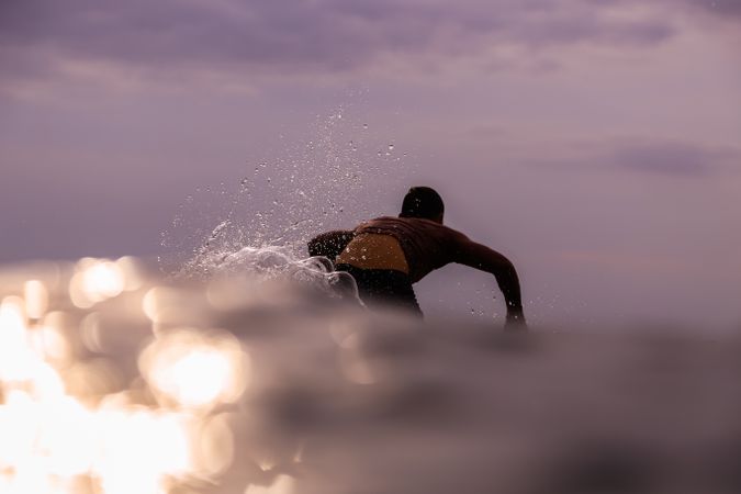 Man on surf board floating on water and cloudy sky