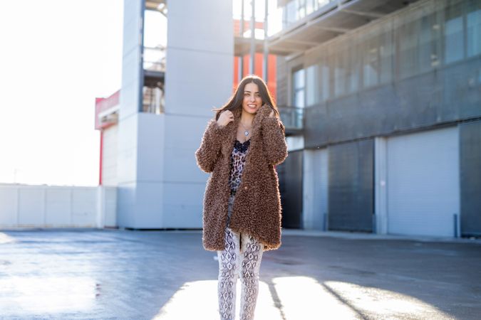 Cheerful woman wrapping in coat on street