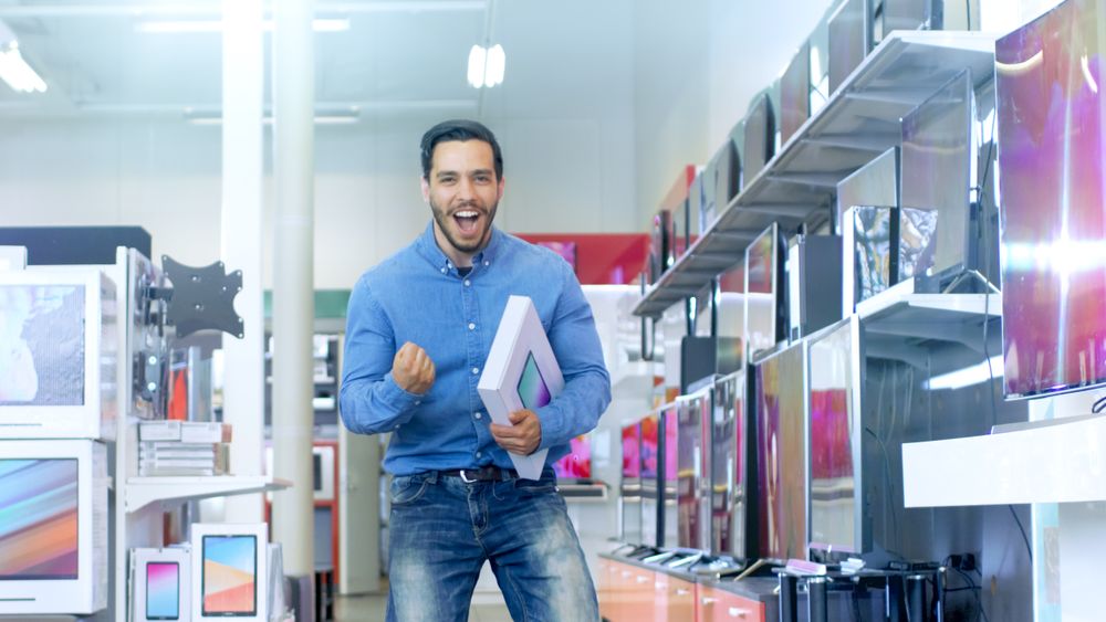 In the Electronics Store Young Man Holds Newly Purchased Computer Tablet  and Happily Jumps with it.