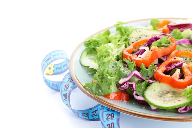 Plate with fresh salad and measuring tape isolated on plain background