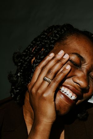 Woman in braids wearing gold ring covering her face smiling