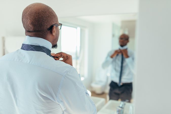 Man putting on a tie looking at a mirror