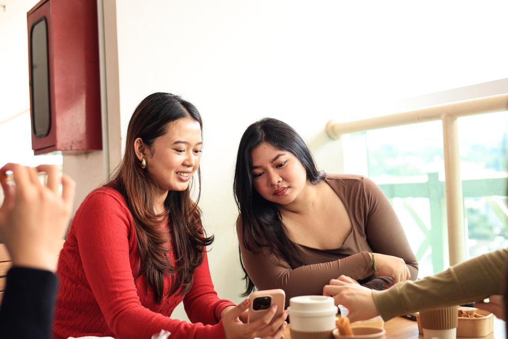 Cheerful Young Asian Women Friends Holding Pink Smartphone Watching Photo Video Using Mobile Apps