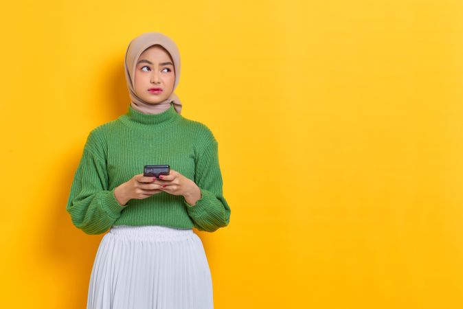 Woman in headscarf holding smart phone and looking away