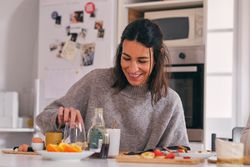 Cheerful woman at table with delicious breakfast in kitchen