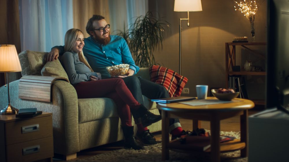 In the Evening Man and Woman are Sitting on the Sofa Watching TV and Eating Popcorn.