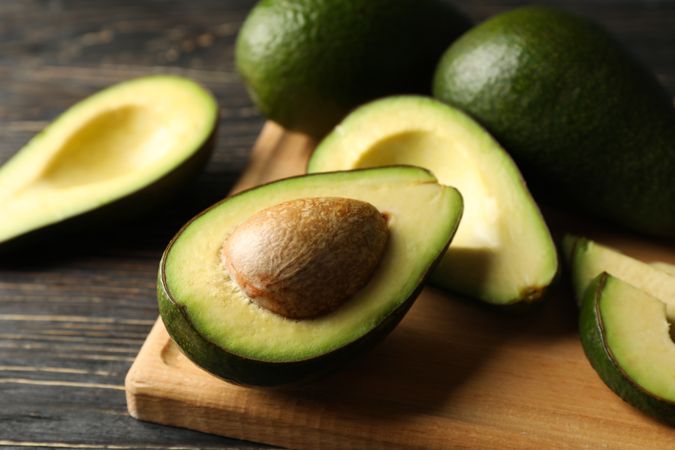 Board with avocado on wooden background, close up