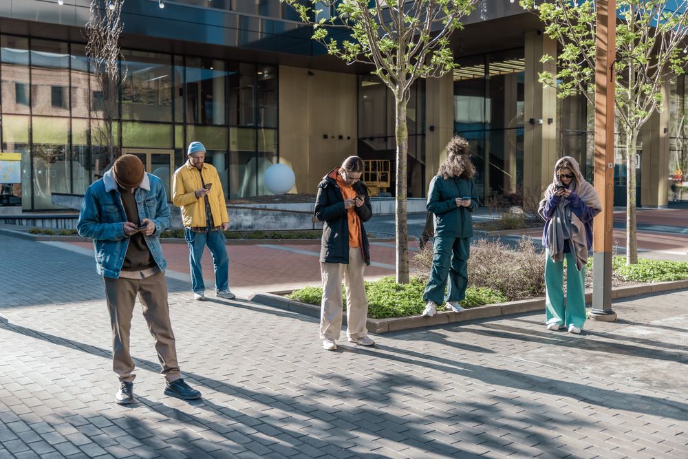 Young Adults Using Smartphones On A City Street, Engaged In Social Media, Posting Content