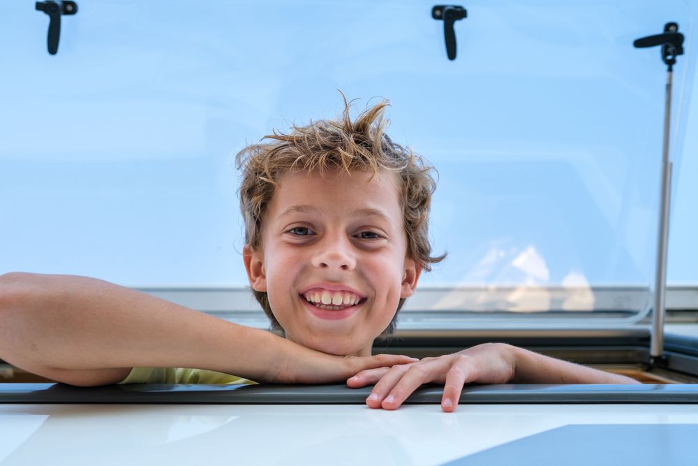 Delighted boy looking at camera from camper window