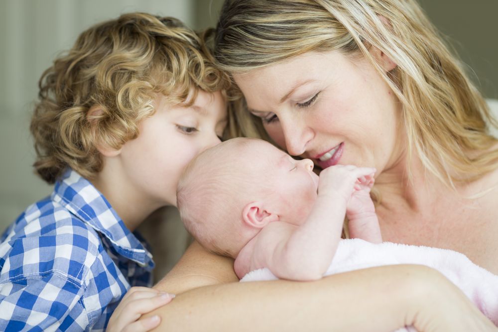 Young Mother Holds Newborn Baby Girl as Brother Looks On