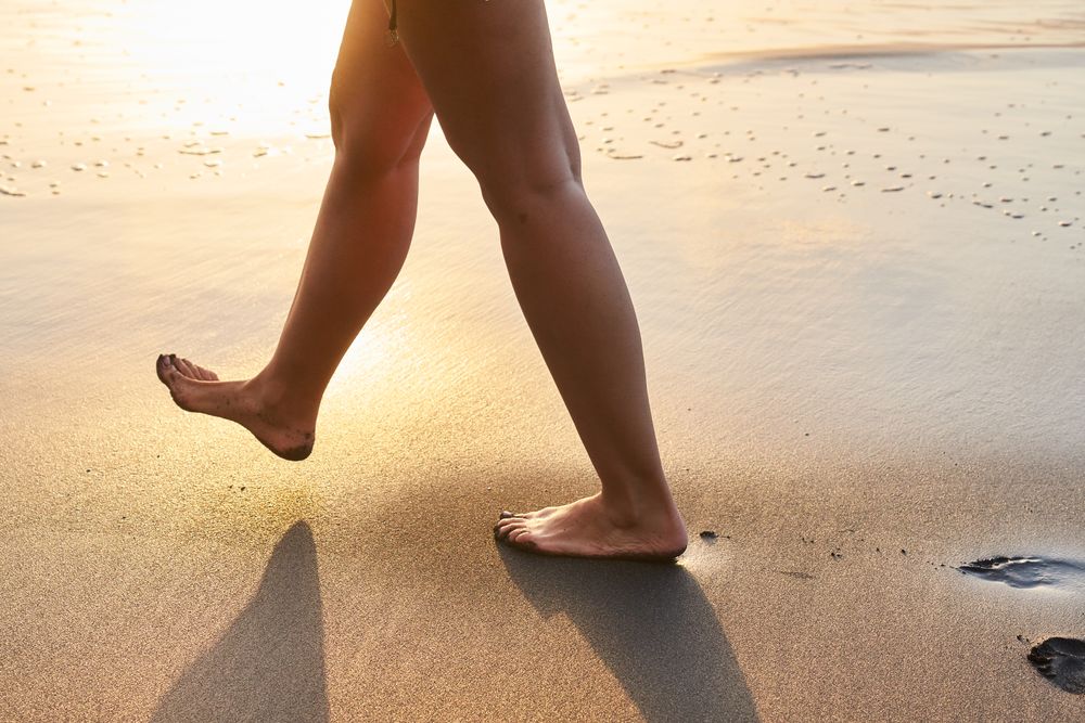Crop woman strolling on sand of beach