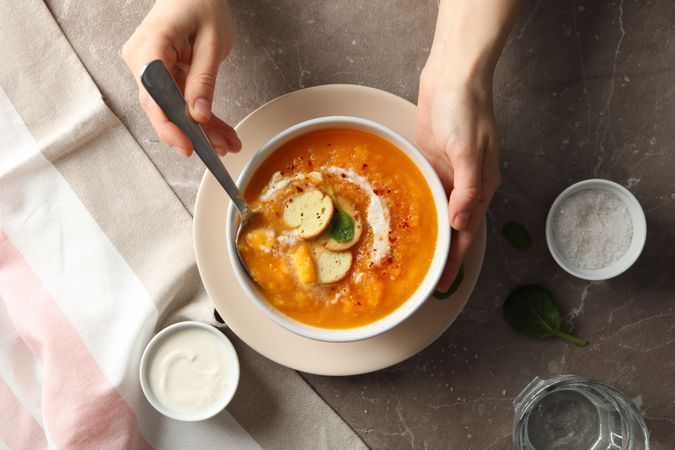 Person’s hands reaching for bowl of pumpkin soup with croutons