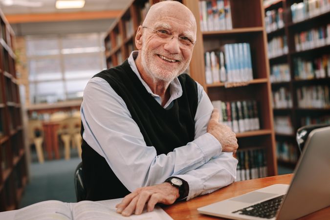 Cheerful older man sitting in library and studying