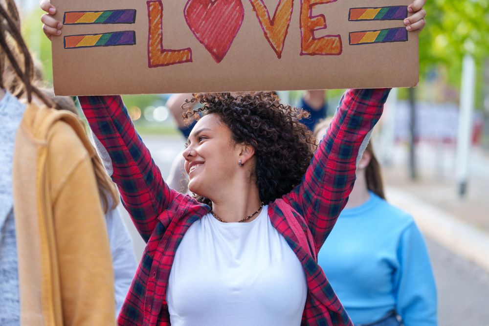 Happy curly-haired woman holding a sign 'Love' during an LGBTQIA rally