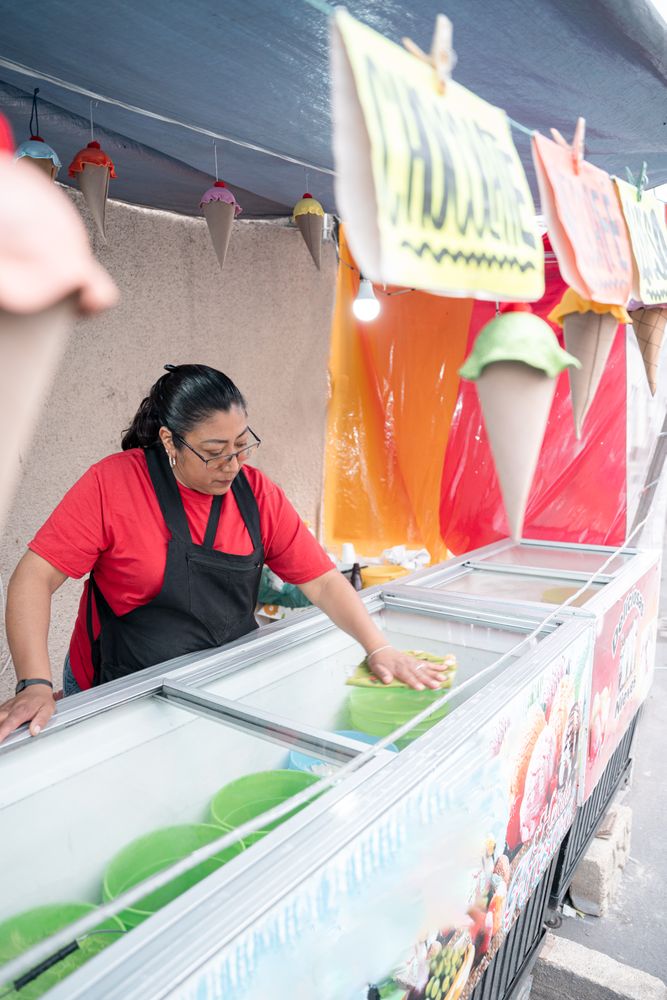 An Hispanic woman is cleaning the ice cream freezer in her street market stall