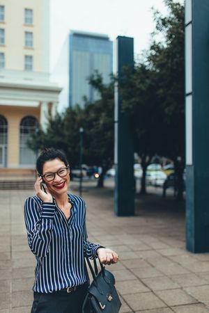 Smiling young asian businesswoman walking outdoors and talking on cell phone