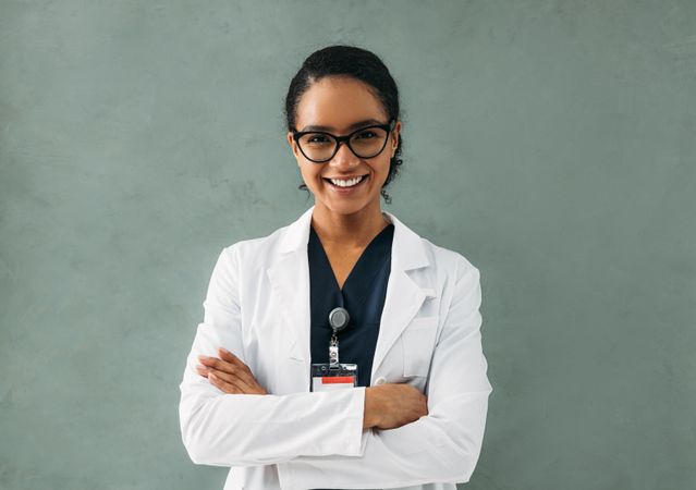 Portrait of smiling female Black doctor in lab coat in grey room